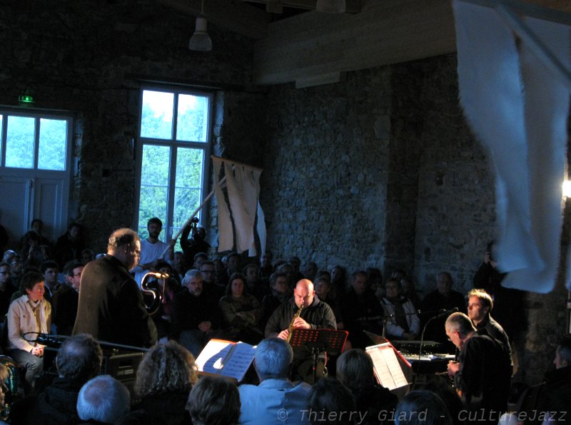 38_ConcertDesParfums_JSLP2012_18mai.JPG - > Vendredi 18 et samedi 19 mai - Salle de la Guérie - "Concert des parfums" Michel Godard / Ursula S YeoMusique et parfums... quelle belle association ! Notes de musique, notes de tête, notes de cœur, les floraux succèdent aux boisés, jazz,  musiques électroniques et musique baroque se mêlent.Accords, notes, harmonie... Parfum et Musique parlent le même langage. La créatrice,  Ursula S Yeo a préalablement créé ses parfums bio à partir des musiques de  Michel Godard et les vaporise en direct sur des bandes de tissu.  Les quatre musiciens, Michel Godard (serpent, tuba et basse ), Gavino Murgia (voix, saxophone), Sébastien Marq (flûtes à bec), et Patrice Héral (percussions, électronique, voix), enivrés par les fragances délectables qui exaltent leur pouvoir créateur, nous invitent à un voyage hors du temps.Dans un lieu adapté où vieilles pierres et bois brut créent déjà le climat, il y a quelque chose de cérémonial, de mystique dans ce concert : deux jeunes hommes vêtus de blanc font flotter au-dessus de nos têtes les étendards imprégnées des parfums, boucles sonores et voix d'outre-tombe, on s'emplit de musique et de senteurs...Tout cela est un rien hypnotique...Pour "être au parfum", voilà une expérience musicale et olfactive à ne pas rater.
